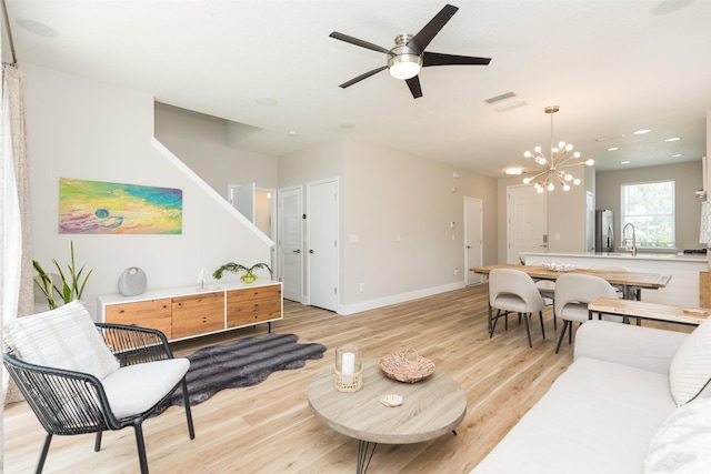 living area with light wood-type flooring, baseboards, and ceiling fan with notable chandelier