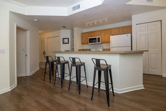 kitchen with dark hardwood / wood-style flooring, white appliances, a kitchen breakfast bar, and a large island