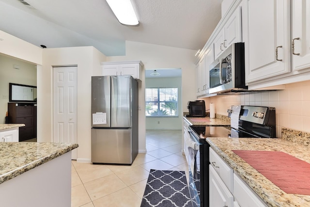 kitchen featuring white cabinetry, stainless steel appliances, lofted ceiling, decorative backsplash, and light tile patterned floors