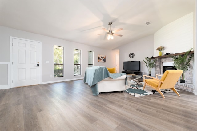 living area with vaulted ceiling, wood finished floors, a ceiling fan, a brick fireplace, and baseboards