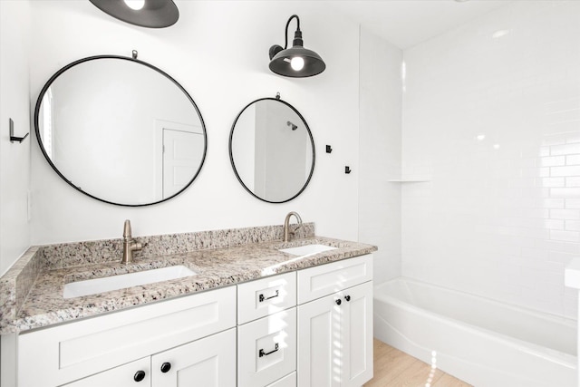 full bath featuring a sink, washtub / shower combination, wood finished floors, and double vanity