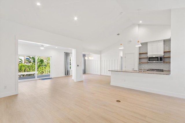 unfurnished living room with a chandelier, light wood-type flooring, high vaulted ceiling, and sink