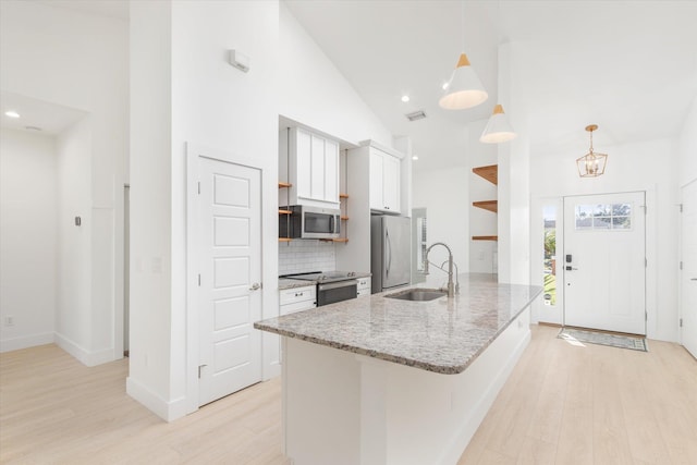 kitchen with light stone countertops, stainless steel appliances, sink, white cabinetry, and hanging light fixtures