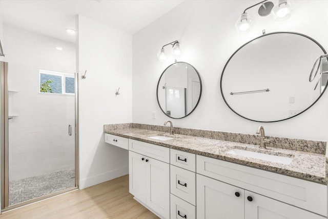 full bathroom featuring double vanity, a shower stall, wood finished floors, and a sink