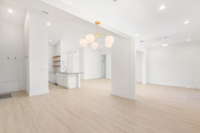 unfurnished living room with ceiling fan with notable chandelier, sink, and light hardwood / wood-style flooring