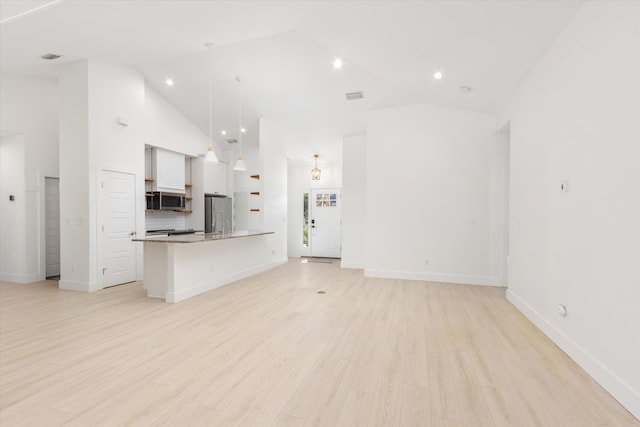 kitchen with decorative light fixtures, a breakfast bar, stainless steel appliances, light wood-style floors, and high vaulted ceiling