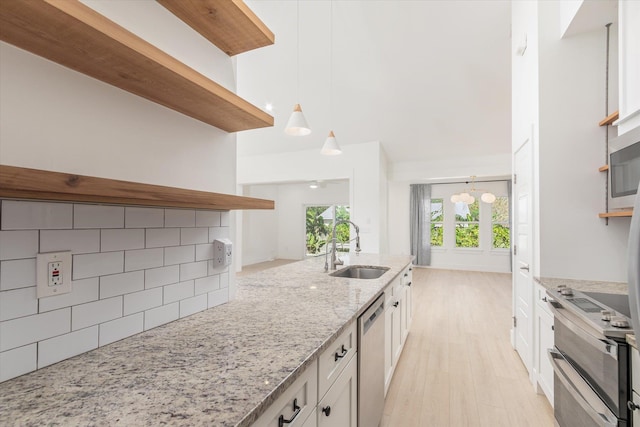 kitchen featuring white cabinetry, sink, light stone counters, pendant lighting, and light hardwood / wood-style floors