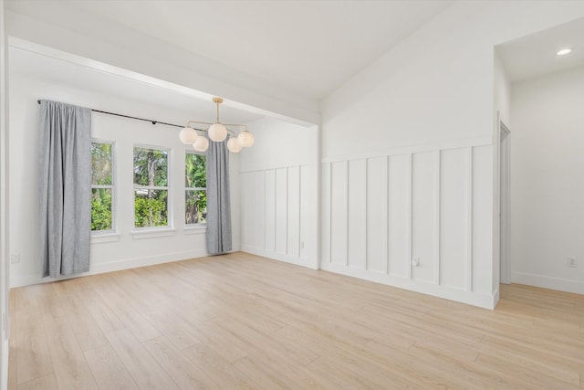 unfurnished room featuring vaulted ceiling, an inviting chandelier, and light hardwood / wood-style flooring