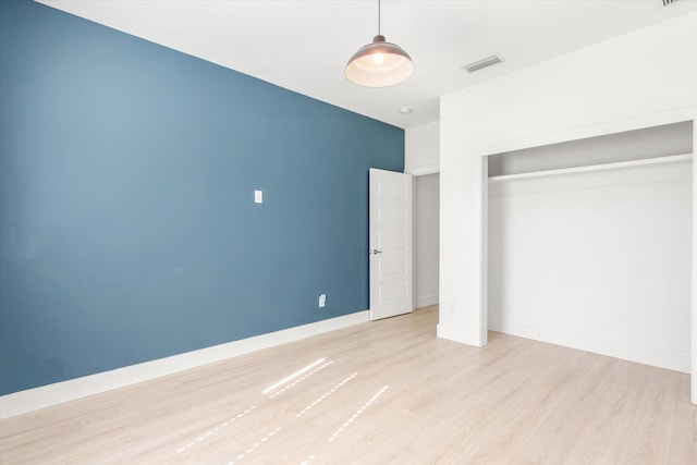 unfurnished bedroom with a closet, visible vents, baseboards, and wood finished floors