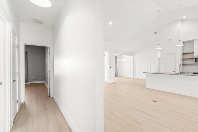 hall featuring baseboards, visible vents, high vaulted ceiling, light wood-style floors, and a chandelier