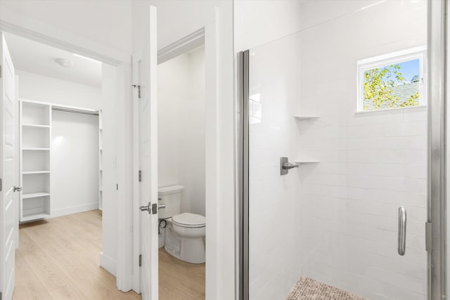 full bathroom featuring a stall shower, a walk in closet, toilet, and wood finished floors