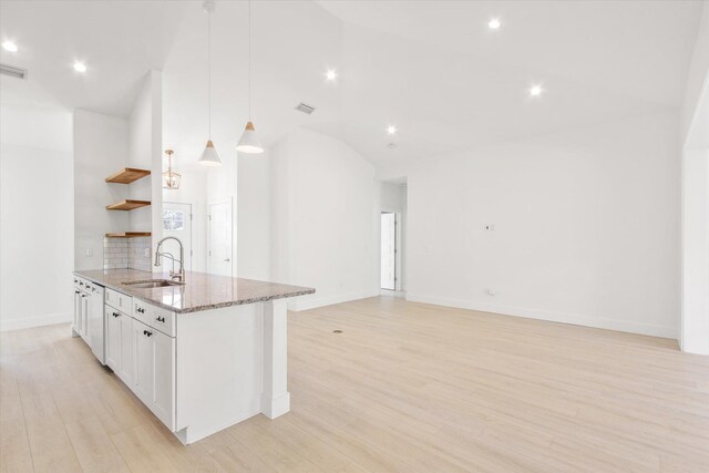 kitchen featuring sink, light wood-type flooring, decorative light fixtures, light stone counters, and white cabinetry