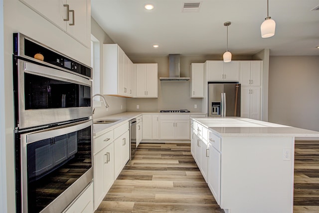 kitchen with wall chimney exhaust hood, sink, decorative light fixtures, a center island, and appliances with stainless steel finishes