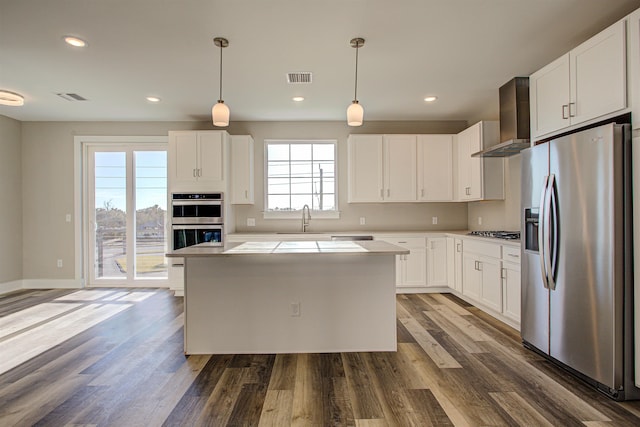 kitchen with wall chimney exhaust hood, hanging light fixtures, appliances with stainless steel finishes, dark hardwood / wood-style flooring, and white cabinets