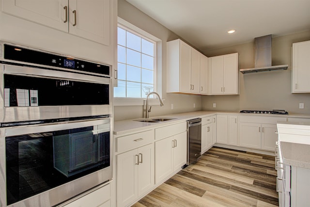 kitchen featuring sink, stainless steel appliances, white cabinets, wall chimney exhaust hood, and light wood-type flooring