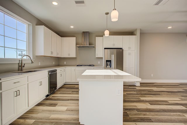 kitchen featuring wall chimney exhaust hood, sink, a center island, hanging light fixtures, and stainless steel appliances