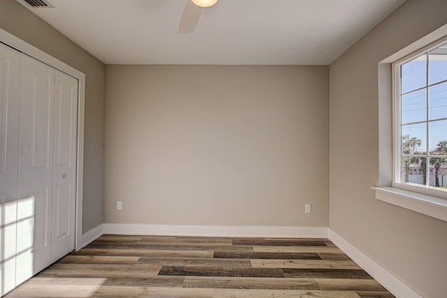 unfurnished bedroom featuring multiple windows, hardwood / wood-style flooring, ceiling fan, and a closet