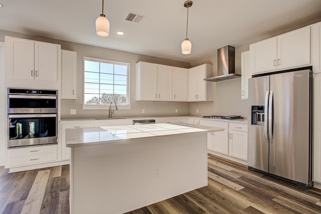 kitchen with wall chimney exhaust hood, stainless steel appliances, a center island, and hanging light fixtures