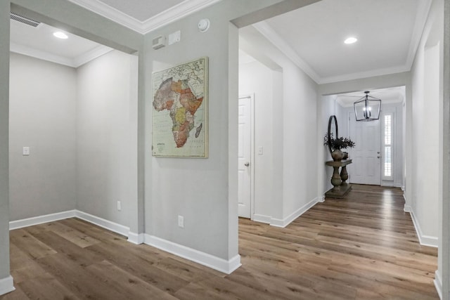 hall with a notable chandelier, ornamental molding, visible vents, and wood finished floors