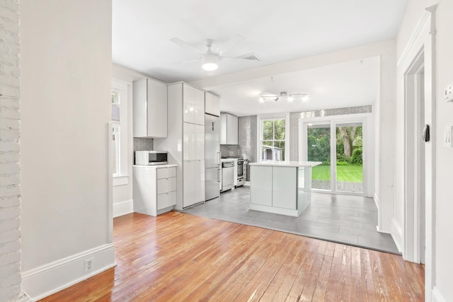 kitchen featuring ceiling fan, white cabinetry, stainless steel appliances, light hardwood / wood-style floors, and decorative backsplash