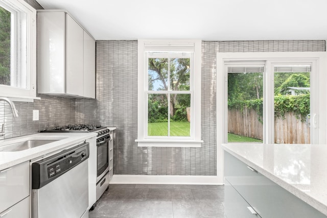 kitchen featuring white cabinetry, light stone countertops, a wealth of natural light, and stainless steel dishwasher