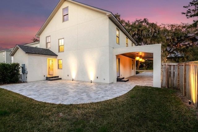 back house at dusk with a patio area and a lawn