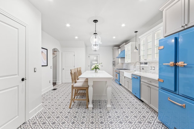 kitchen with white cabinetry, hanging light fixtures, stainless steel appliances, range hood, and tasteful backsplash