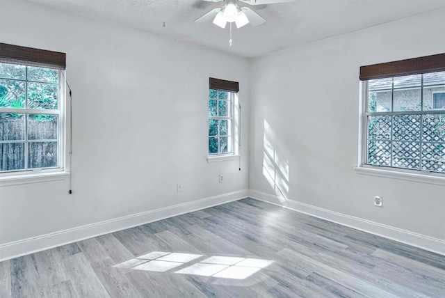 empty room with a healthy amount of sunlight, a ceiling fan, light wood-style flooring, and baseboards