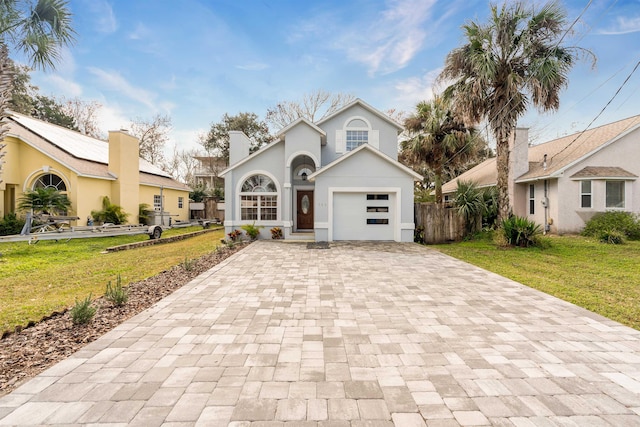 view of front of property featuring stucco siding, decorative driveway, fence, a front yard, and a garage