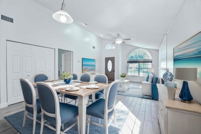 dining area featuring visible vents, light wood-style floors, ceiling fan, and high vaulted ceiling