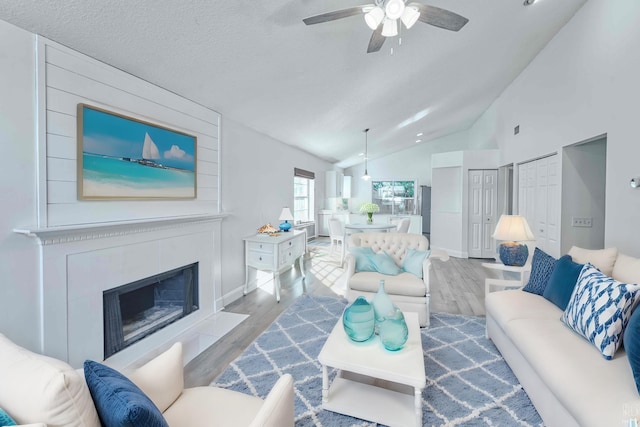 living area with wood finished floors, a ceiling fan, lofted ceiling, a fireplace with flush hearth, and a textured ceiling