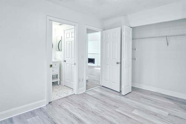 unfurnished bedroom featuring a closet, baseboards, light wood-style floors, and ensuite bathroom