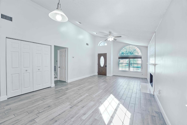 unfurnished living room with visible vents, ceiling fan, a fireplace, light wood-style floors, and a textured ceiling