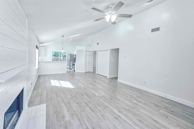 unfurnished living room with visible vents, ceiling fan, high vaulted ceiling, light wood-style floors, and a textured ceiling