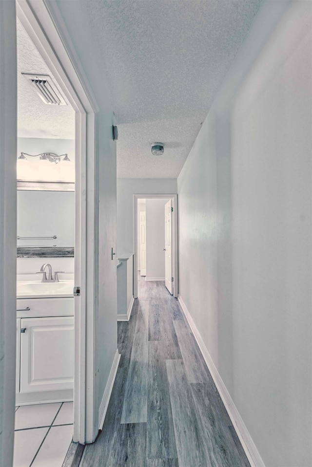 hallway featuring visible vents, a sink, a textured ceiling, wood finished floors, and baseboards