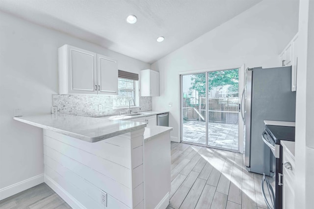 kitchen featuring wood finish floors, a sink, tasteful backsplash, appliances with stainless steel finishes, and vaulted ceiling