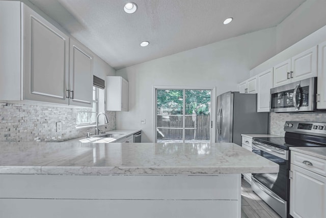 kitchen featuring a sink, appliances with stainless steel finishes, white cabinets, and vaulted ceiling