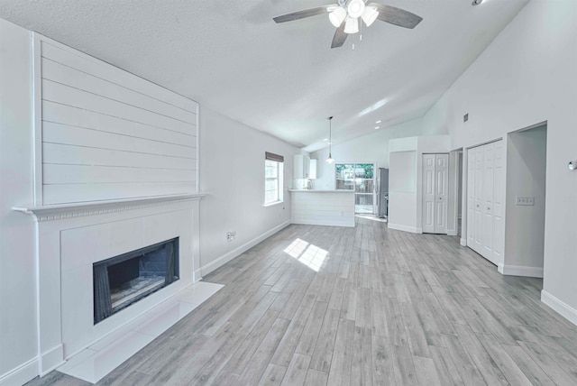 unfurnished living room featuring light wood-type flooring, a textured ceiling, a fireplace, baseboards, and ceiling fan