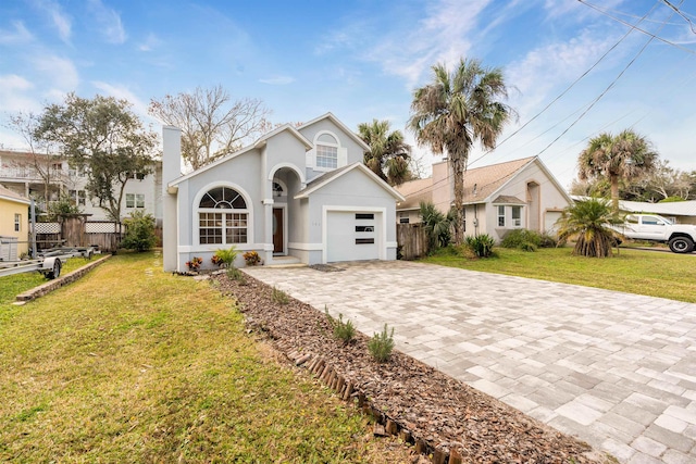 view of front facade featuring stucco siding, a front lawn, decorative driveway, fence, and a garage