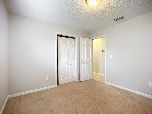 unfurnished bedroom featuring light colored carpet, a closet, and a textured ceiling