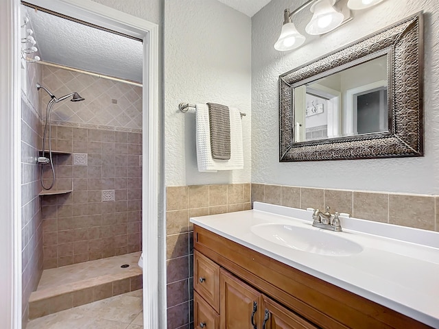 bathroom with tile patterned flooring, vanity, tiled shower, and tile walls