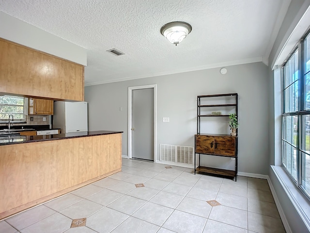 kitchen with tasteful backsplash, white fridge, light tile patterned floors, crown molding, and a textured ceiling