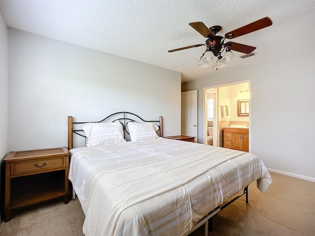 bedroom featuring ceiling fan, ensuite bathroom, light carpet, and a textured ceiling