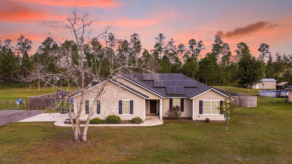 single story home with a lawn, solar panels, a shed, and a patio