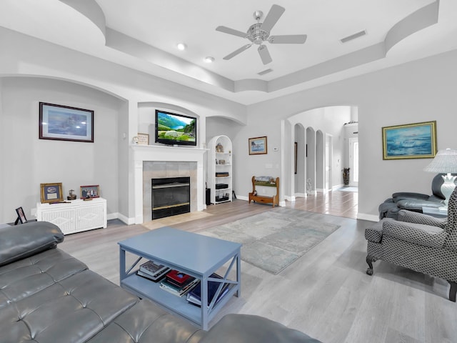1201 Ellington Ct, Saint Augustine, FL 32084 - living room featuring arched walkways, a ceiling fan, a tray ceiling, a tiled fireplace, and wood finished floors