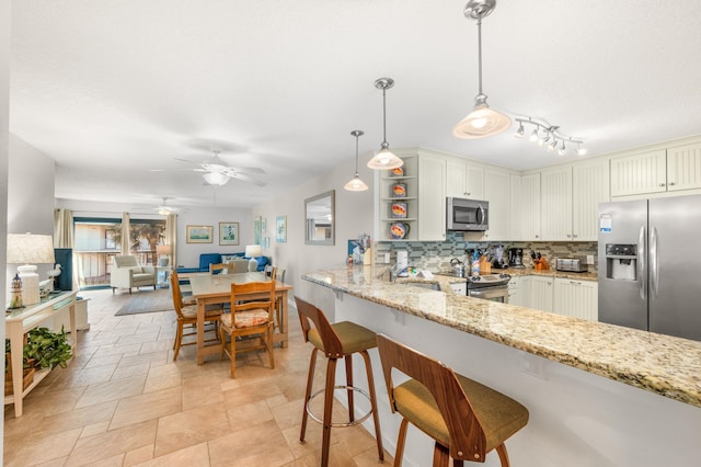 kitchen with hanging light fixtures, tasteful backsplash, light stone counters, kitchen peninsula, and stainless steel appliances