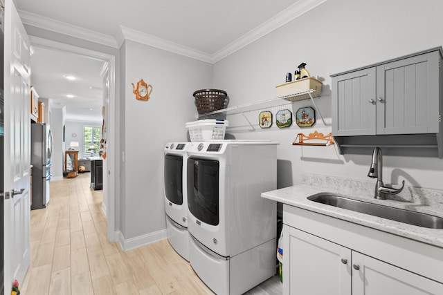 clothes washing area featuring washing machine and clothes dryer, cabinet space, a sink, baseboards, and ornamental molding