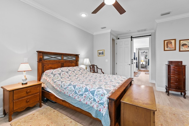 bedroom featuring a barn door, ornamental molding, light wood-style flooring, and visible vents