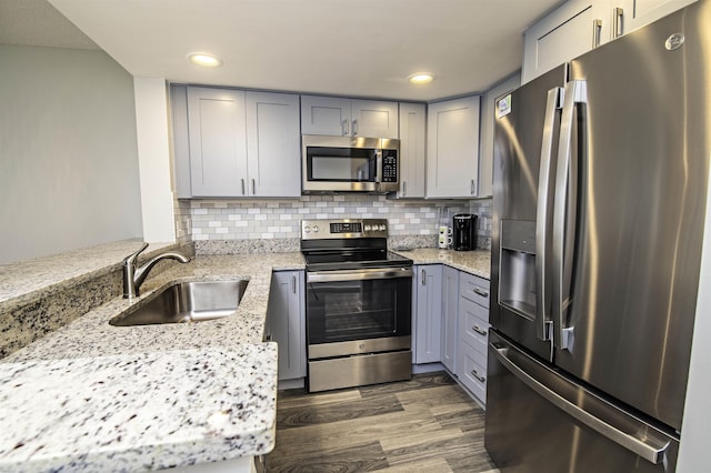 kitchen featuring appliances with stainless steel finishes, light stone counters, sink, gray cabinets, and dark hardwood / wood-style floors