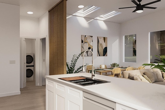 kitchen featuring stacked washer and clothes dryer, sink, light wood-type flooring, white dishwasher, and white cabinets